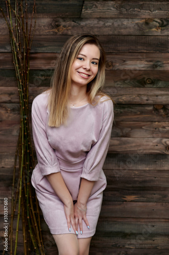 Loft style concept. Portrait of a beautiful smiling girl in a pink pretty dress on a background of interior in a room made of wood. Shows happiness, smile, kindness. Standing in front of the camera.
