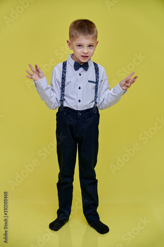 Portrait of a cute 10 years old schoolboy boy on a yellow background. Standing straight at full height, Showing emotions, talking.