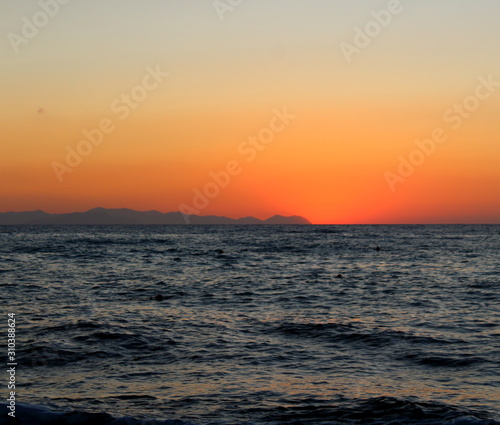 the sun setting behind the promontory with the sea in the foreground