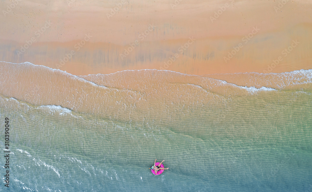 Aerial top view from drone, View of boy with swim ring in the sea and shade emerald blue water and wave foam at sunrise