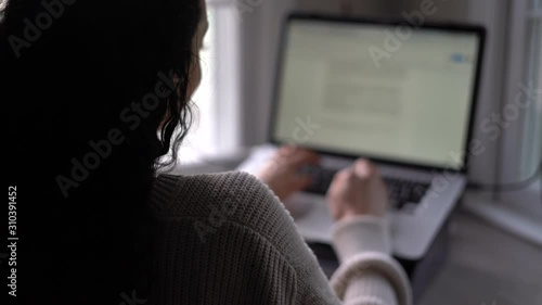 Young woman typing quickly on a laptop computer or tablet with a keyboard - view from behind