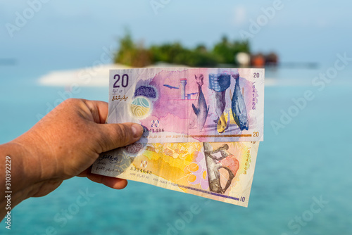 A tourist's show Maldivian rufiyaa bank note when she traveling in Maldives. Money of Maldives bank note in female's hand on the background of the island, salary incomes. photo