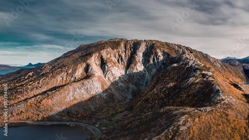 A drone hyperlapse. A view of the mountain, fjord, and the valley near the Kjelling, Norway. The mountain is coved in the dense forest, the road is following the coastline,  thick clouds above. photo