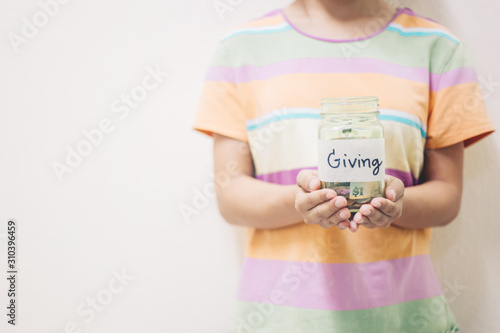 Hand putting Coins in glass jar with Giving word written text label for giving and donation concept