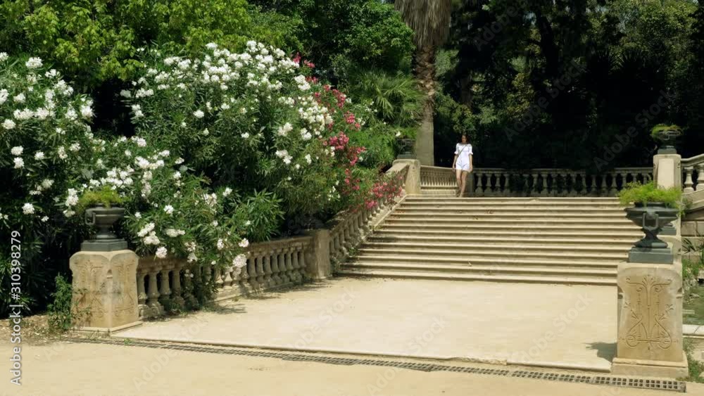 Scenery shot of happy beautiful girl walking in the blooming summer park and going down the stairs. Barcelona. Spain. 4K Scenery shot of happy beautiful girl walking in the blooming summer park and going down the stairs. Barcelona. Spain. 4K