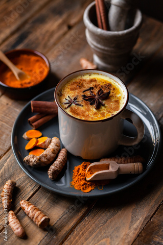 Golden milk in white mug, turmeric latte made with curcuma, cinnamon, anise, honey. Healthy hot winter drink, natural, organic beverage. Close up, front view.  Wooden rustic background