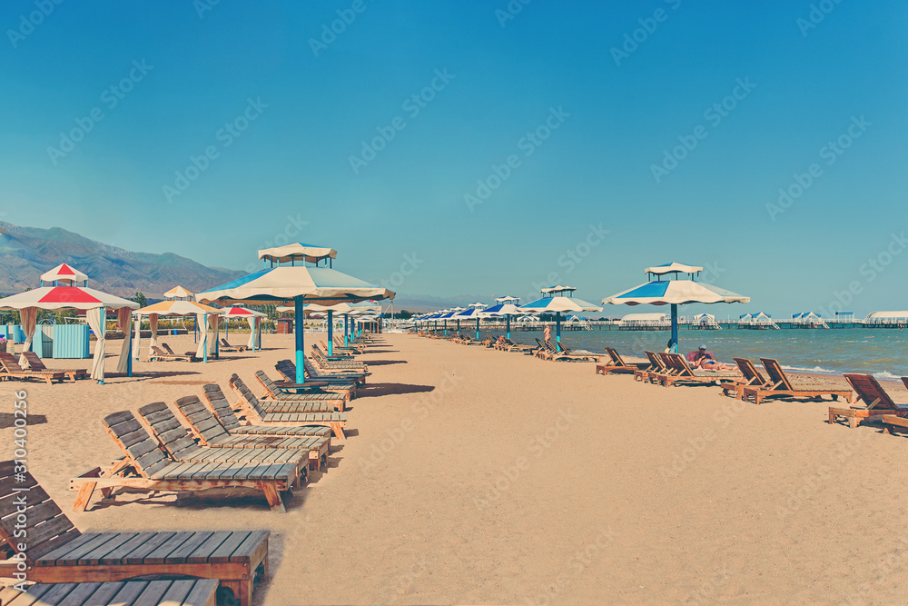 Sunbeds on the beach. A row of sun umbrellas with seats on the lake shore.