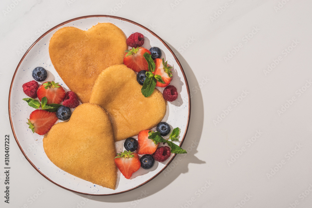 top view of tasty heart shaped pancakes with berries and mint on white background top view of tasty heart shaped pancakes with berries and mint on white background