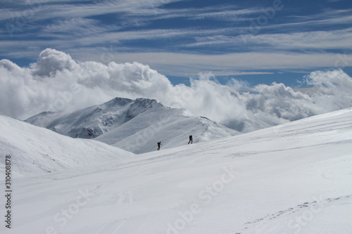 dos esquiadores subiendo por la ladera de una montaña con nubes al fondo