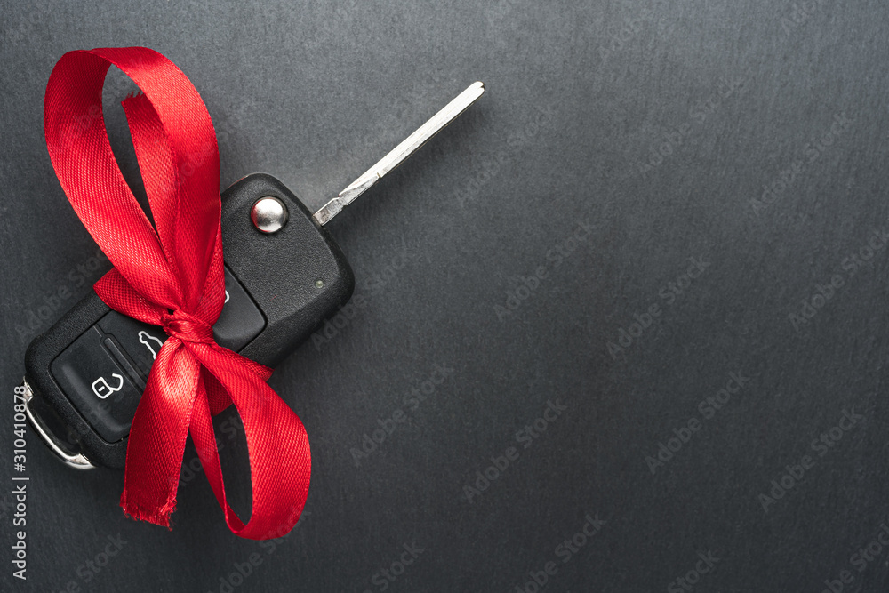 Car key with red bow on dark black slate plate background. Christmas or Valentine's Day gift or present abstract concept. Copy space on the left. Flat lay top view.