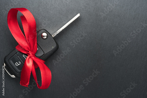 Obraz na płótnie Car key with red bow on dark black slate plate background. Christmas or Valentine's Day gift or present abstract concept. Copy space on the left. Flat lay top view. w salonie