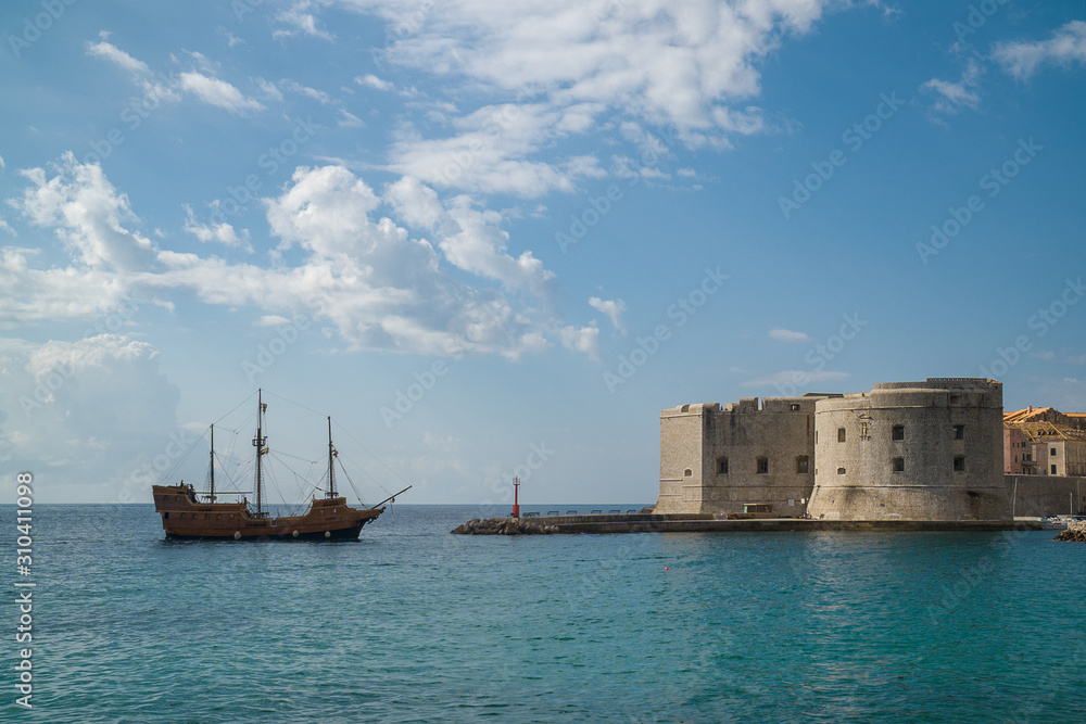 Vintage ship approaching the dock of an old town with medieval fortress