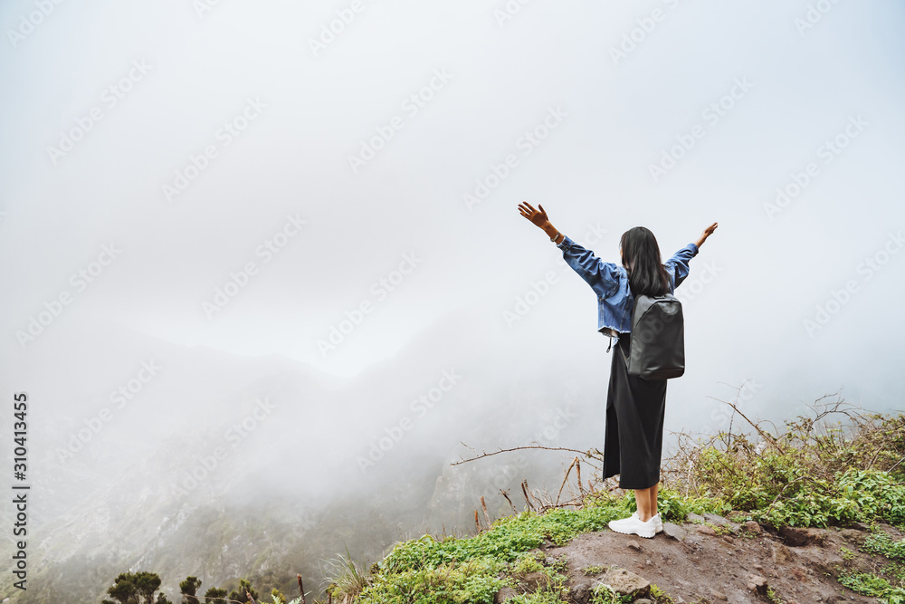 Young woman tourist with backpack relaxing on top of a mountain and enjoying the view of the misty valley Young woman tourist with backpack relaxing on top of a mountain and enjoying the view of the misty valley