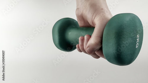 Closeup of hand holding a green dumbbell while exercising and working out for more active lifestyle with hand coming from above the image on a white background