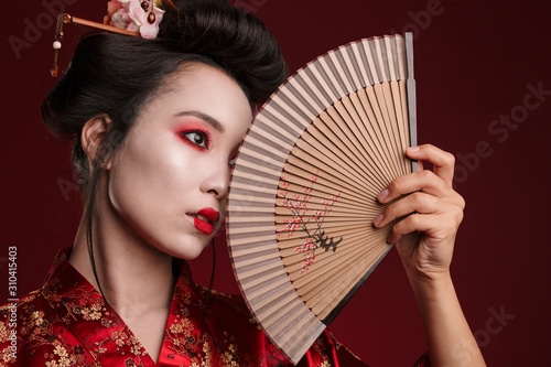 Image of young geisha woman in japanese kimono holding wooden hand fan