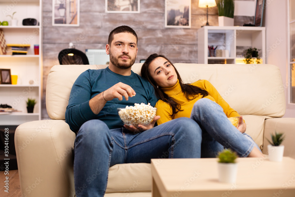 Obraz premium Handsome couple at home eating pop corn and watching TV
