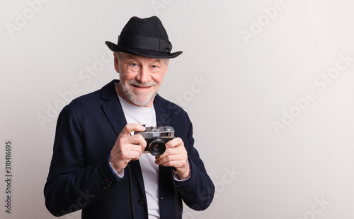 Portrait of a senior man with hat and camera in a studio.