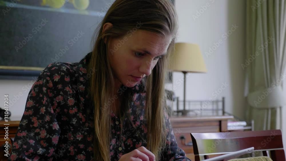 Attractive young woman using tablet while sitting at a table in a classically furnished house in natural lighting, close up Attractive young woman using tablet while sitting at a table in a classically furnished house in natural lighting, close up