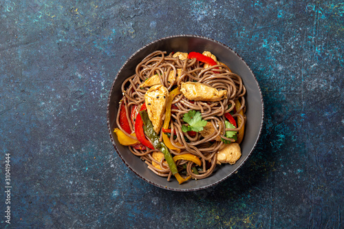 Japanese dish buckwheat soba noodles with chicken and vegetables carrot, bell pepper and green beans in grey bowl, top view, copy space