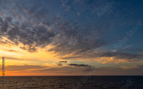 Sunset and dramatic set of clouds drifting over the tropical waters of the Caribbean Sea are lit by the last moments of daylight