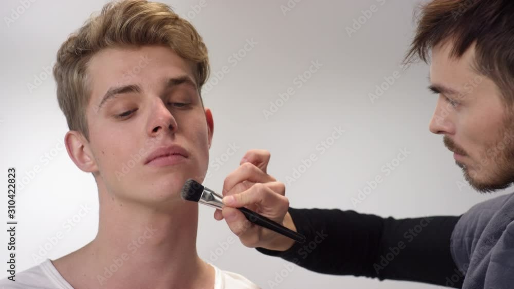 Close up of handsome male beautician applying foundation primer on young Caucasian man neck Close up of handsome male beautician applying foundation primer on young Caucasian man neck