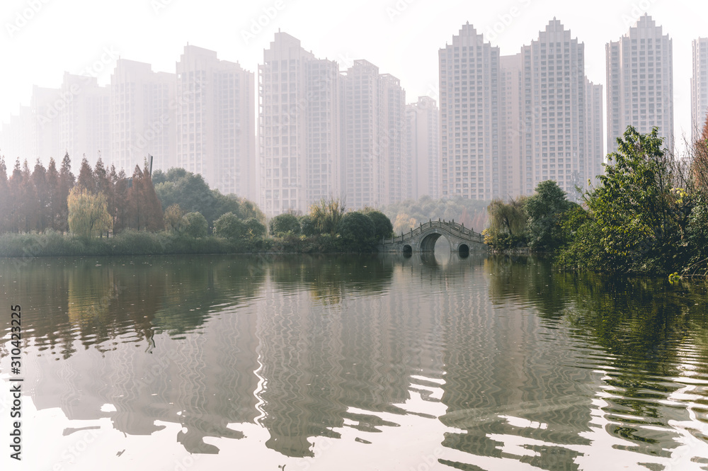 The traditional Chinese architecture semicircle bridge over the Fuhe and Jiangan rivers in the Nanhu Wetland park of Chengdu, Sichuan, China. High-rise apartment buildings on background. Air pollution
