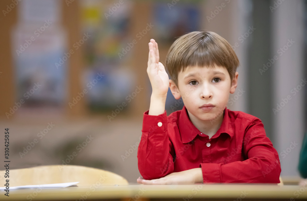 Primary school child raised his hand.A boy in a red shirt at school at his desk.