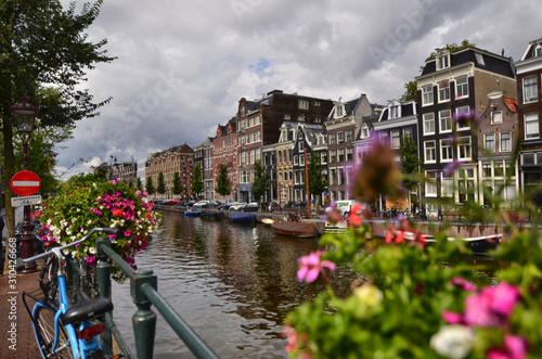 Amsterdam,Holland,August 2019. Enchanting view of a canals of the historic center. The typical houses overlook the water, boats moored along the canal. Planters on railings and bikes. Sunny day.