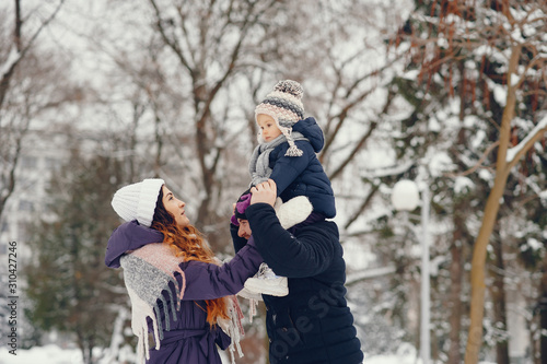 Family have fun in a winter park. Stylish mother in a purple jacket. Little girl in a winter clothes. Father with cute daughter
