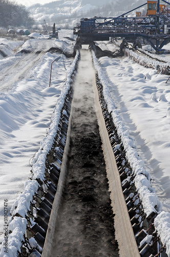 Coal on conveyor belt in winter conditions. Open-pit coal mine covered with snow.