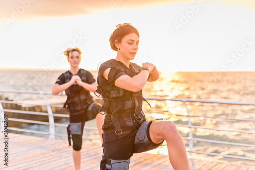 Women with her instructor training in EMS trainer on seaside at sunrise