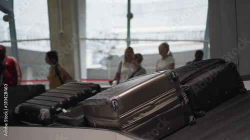 Large number of suitcases and bags of different colors move along the conveyor belt at the airport. Endless baggage flow. Silhouettes of passengers, people waiting for their luggage in the background.