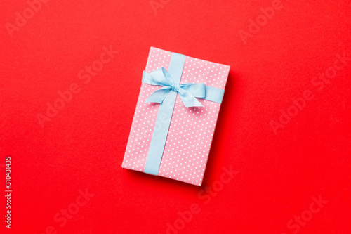 wrapped Christmas or other holiday handmade present in paper with blue ribbon on red background. Present box, decoration of gift on colored table, top view with copy space © sosiukin