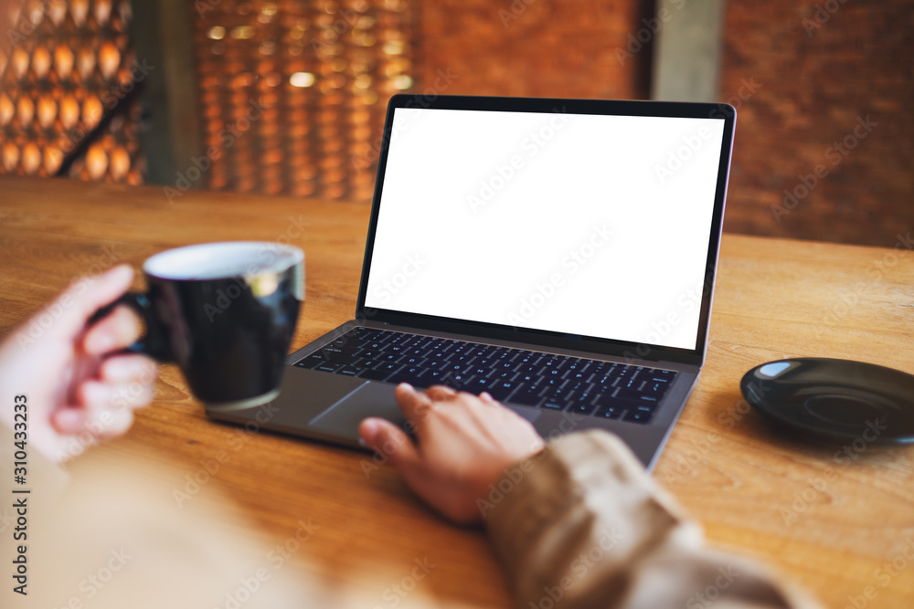 Fototapeta premium Mockup image of a woman using and touching on laptop touchpad with blank white desktop screen while drinking coffee