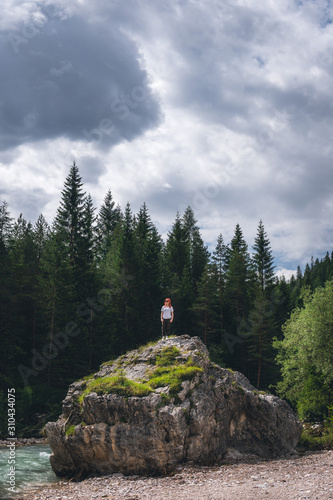 Girl on a large stone  a boulder  among the incredibly beautiful river of turquoise color  pine forest. summer day. vertical photo. Dolomites mountains  Camping Olympia Fiames  Cortina Ampezzo Italy.