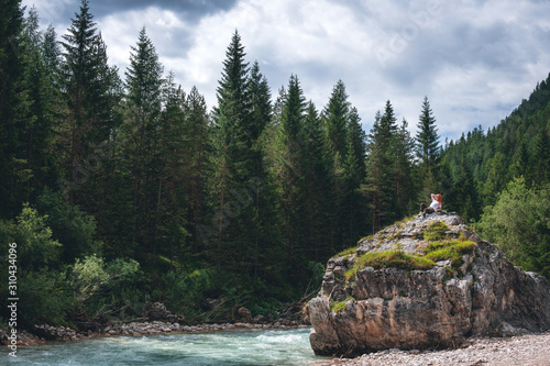 Girl on a large stone, a boulder, among the incredibly beautiful river of turquoise color, pine forest. summer day. Dolomites mountains, Camping Olympia Fiames, Cortina Ampezzo Italy. copy space photo