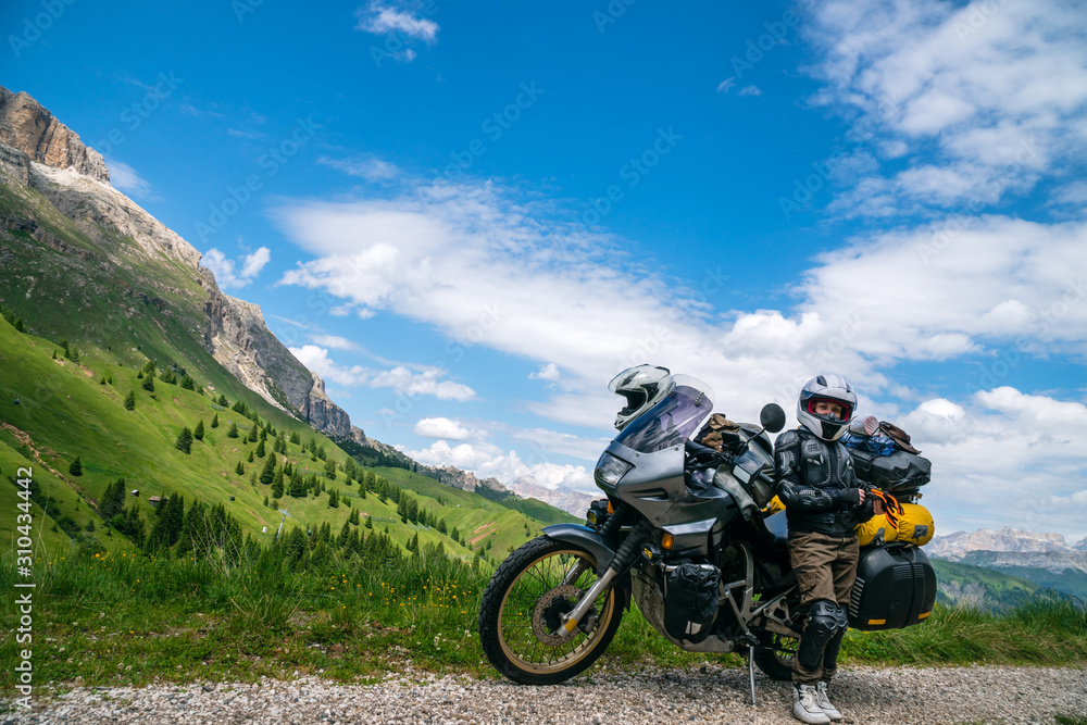 Motorcycle lady standing with adventure motorbike on the top mountain, enduro, off road, beautiful view, danger road in mountains, freedom, extreme vacation. Copy space. Passo Pordoi, Italy Motorcycle lady standing with adventure motorbike on the top mountain, enduro, off road, beautiful view, danger road in mountains, freedom, extreme vacation. Copy space. Passo Pordoi, Italy
