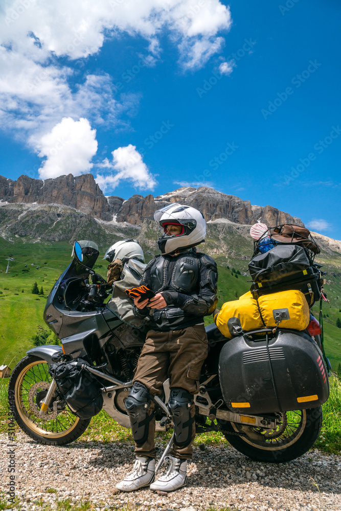 Motorcycle lady standing with adventure motorbike on the top mountain, enduro, off road, beautiful view, danger road in mountains, freedom, extreme vacation. vertical photo. Passo Pordoi, Italy