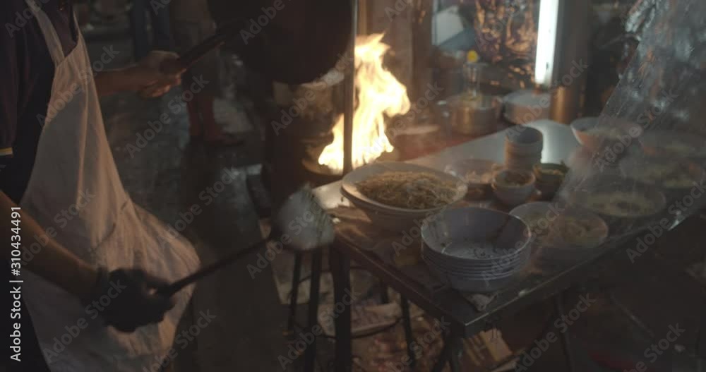 Chinese cook is cooking fired noodles with fire in Bangkok Chinatown at the thai street food market - Close up Chinese cook is cooking fired noodles with fire in Bangkok Chinatown at the thai street food market - Close up