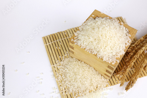 Japanese rice in a wooden box and grains of rice on the White Blackground.