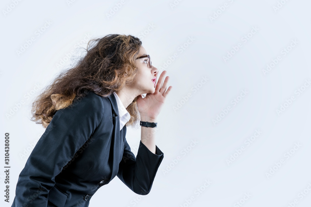 young pretty businesswoman profile view, looking happy and excited, shouting and calling to copy space on the side against a gray wall. Copy space young pretty businesswoman profile view, looking happy and excited, shouting and calling to copy space on the side against a gray wall. Copy space