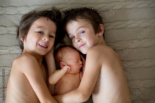 Konstfotografi Two children, toddler and his big brother, hugging and kissing their newborn bab