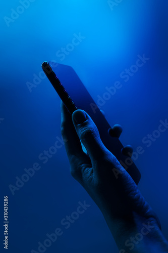 Hand holds smartphone. Neon classic blue light, vertical photo. Copyspace. Technology concept, future, social networks, content, mobile.