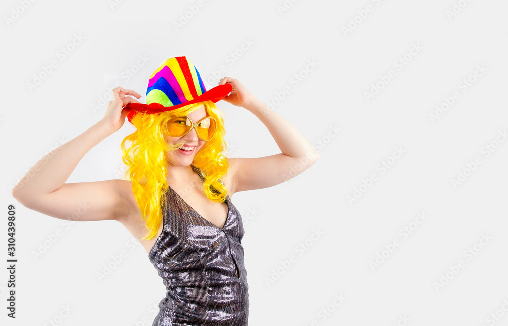 A young lady in a multi-colored carnival cowboy hat, carnival glasses is looking at the camera. Isolated on a gray background. Copy pace A young lady in a multi-colored carnival cowboy hat, carnival glasses is looking at the camera. Isolated on a gray background. Copy pace