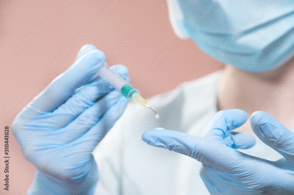 A professional cosmetologist doctor holds in his hand a syringe with anti-aging fluid. A hanging drop on the end of a needle with a filler over a gloved doctor finger. A professional cosmetologist doctor holds in his hand a syringe with anti-aging fluid. A hanging drop on the end of a needle with a filler over a gloved doctor finger.