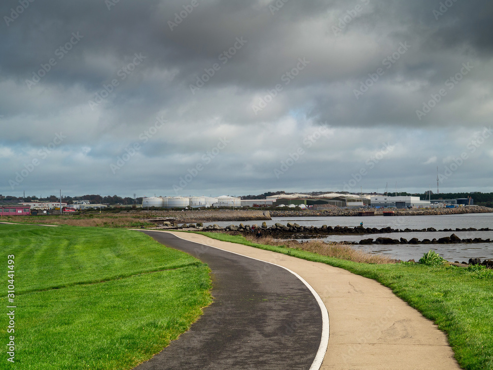Path for walking and cycling in South park, Galway city, Ireland, Port and commercial buildings in the background, Cloudy low sky.