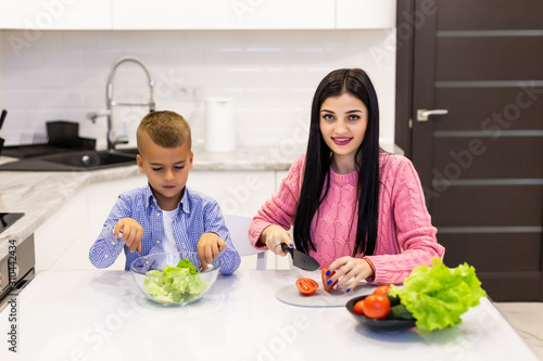 Young mother with son boy cooking salad mom sliced vegetables food son tasting salad. Happy family cook food enjoyment lifestyle kitchen