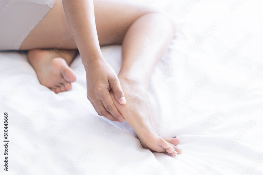 Close up woman touching her leg with pain lying on white bed, health care concept
