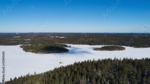 Aerial view of a white snowy lake in winter, clouds on a blue sky create shadows on the surface at sunny day. Beautiful landscape of northern nature with drone.