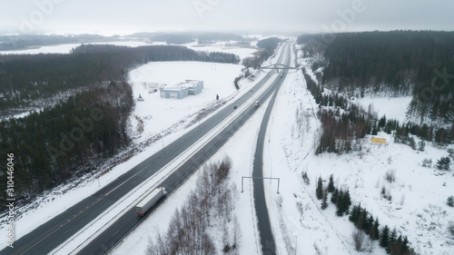 Freeway passing through the winter forest. The road with cars goes away to the horizon line. Aerial view.